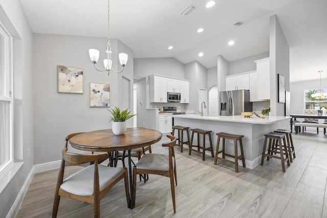 dining area with light wood-type flooring, high vaulted ceiling, sink, and a notable chandelier