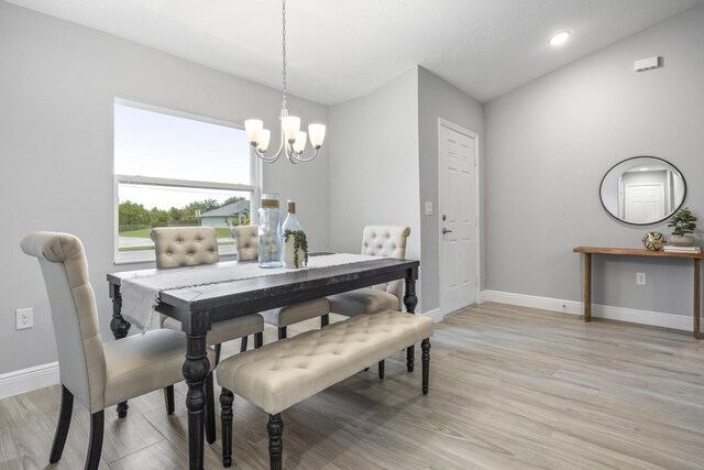 dining area with light hardwood / wood-style floors, vaulted ceiling, and an inviting chandelier