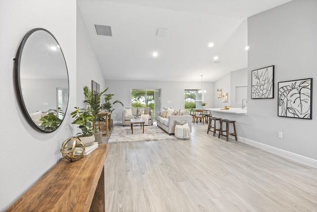 living room with high vaulted ceiling, sink, and light hardwood / wood-style floors