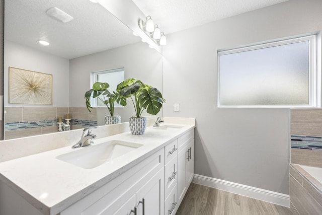 bathroom featuring wood-type flooring, tiled bath, vanity, and a textured ceiling