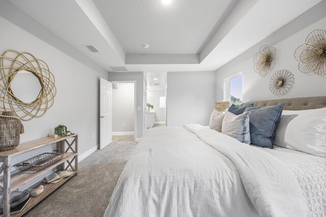 bedroom featuring carpet flooring, ensuite bathroom, and a tray ceiling