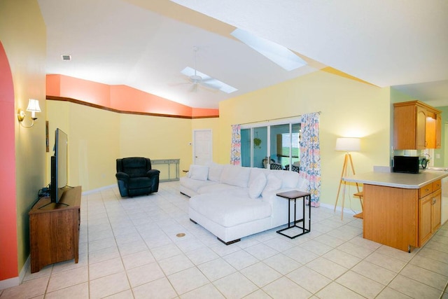 living room with ceiling fan, lofted ceiling with skylight, and light tile patterned floors