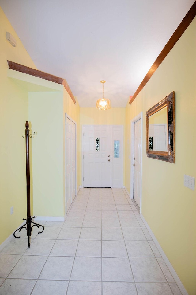 corridor with crown molding, light tile patterned floors, and an inviting chandelier