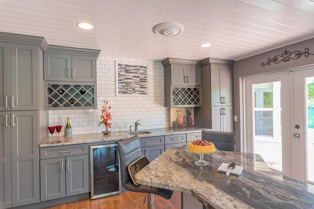 kitchen with decorative backsplash, light wood-type flooring, light stone counters, and beverage cooler