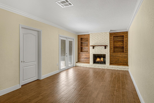 unfurnished living room with hardwood / wood-style floors, crown molding, a brick fireplace, built in shelves, and a textured ceiling