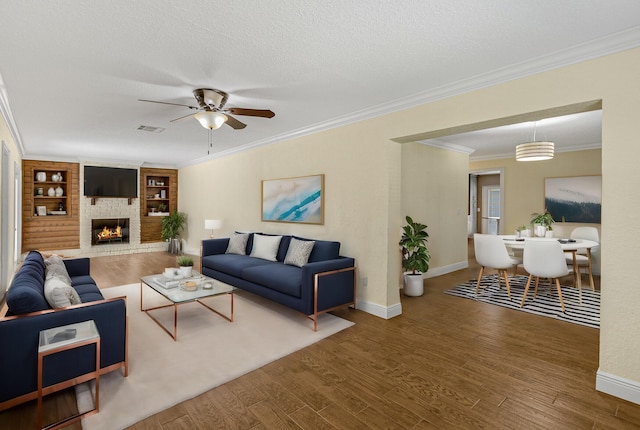 living room featuring hardwood / wood-style floors, crown molding, a brick fireplace, ceiling fan, and built in features