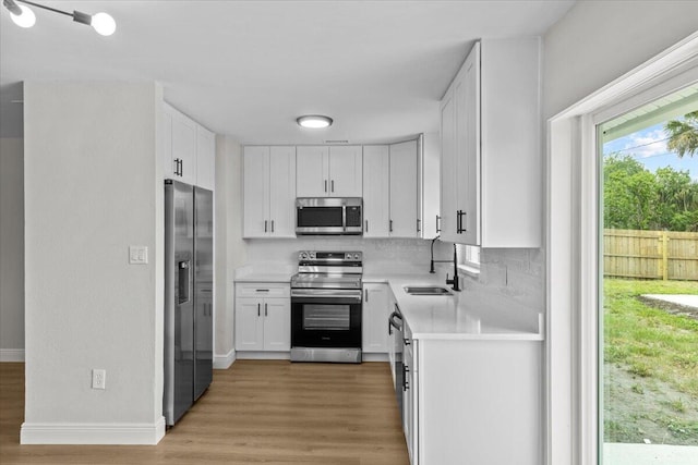 kitchen with sink, decorative backsplash, light wood-type flooring, white cabinetry, and stainless steel appliances