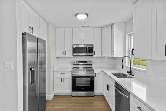 kitchen with wood-type flooring, stainless steel appliances, white cabinetry, and sink