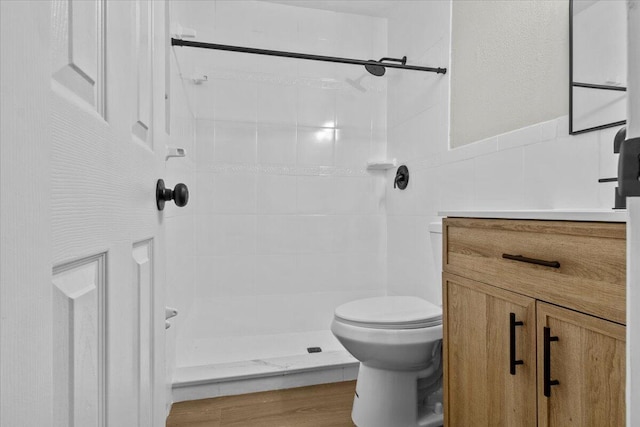 bathroom featuring hardwood / wood-style flooring, vanity, toilet, and tiled shower