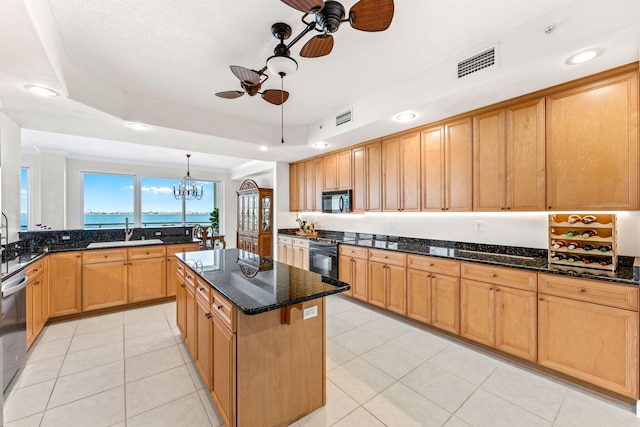 kitchen with dark stone counters, sink, black appliances, decorative light fixtures, and a center island