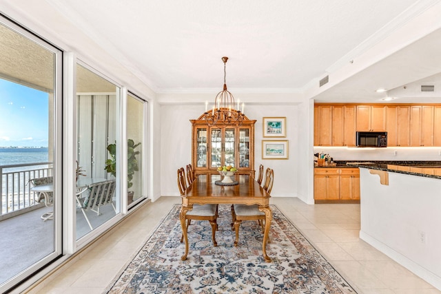 dining space with light tile patterned floors, a water view, an inviting chandelier, and ornamental molding