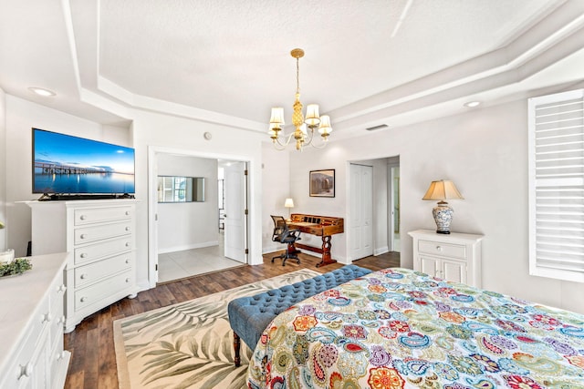 bedroom with a chandelier, dark hardwood / wood-style flooring, a raised ceiling, and connected bathroom