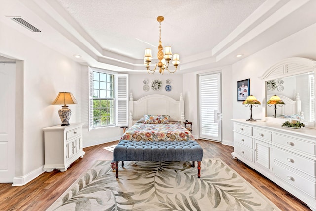 bedroom with a notable chandelier, dark hardwood / wood-style flooring, a raised ceiling, and a textured ceiling