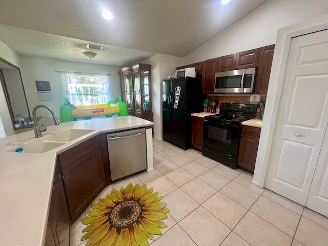 kitchen with kitchen peninsula, sink, black appliances, light tile patterned floors, and lofted ceiling