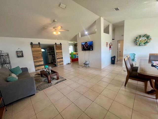 living room featuring a barn door, ceiling fan, light tile patterned floors, and a textured ceiling