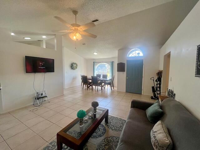 tiled living room with ceiling fan, lofted ceiling, and a textured ceiling