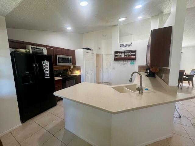 kitchen featuring black appliances, kitchen peninsula, sink, and light tile patterned floors