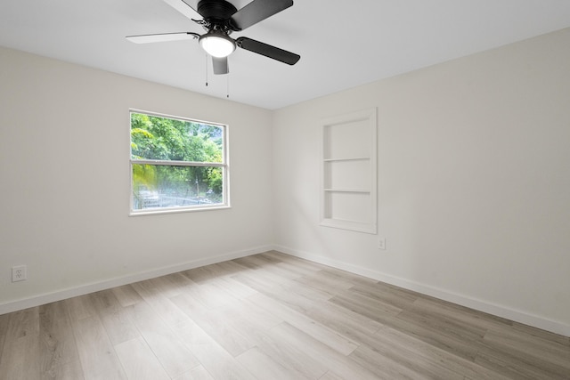 empty room featuring built in shelves, light hardwood / wood-style flooring, and ceiling fan