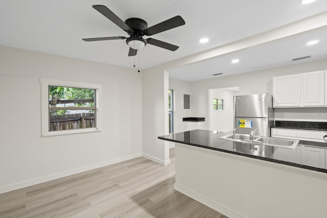 kitchen featuring stainless steel fridge, sink, white cabinetry, and dark stone countertops