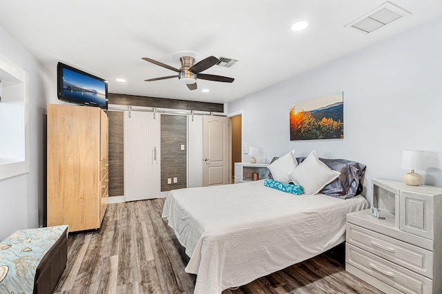 bedroom featuring wood-type flooring, a barn door, and ceiling fan