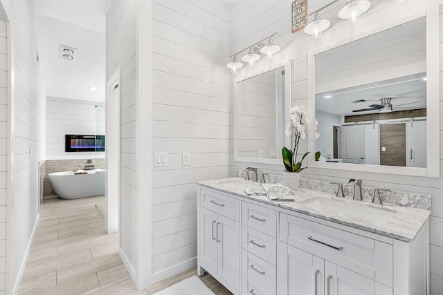 bathroom with a textured ceiling, dual vanity, ceiling fan, and wood walls