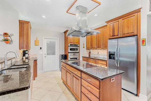 kitchen featuring stainless steel appliances, island exhaust hood, tasteful backsplash, dark stone countertops, and sink