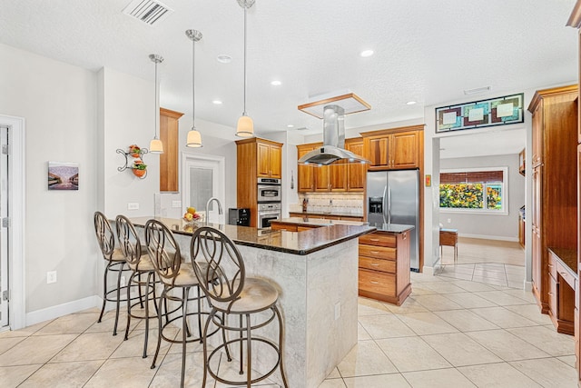 kitchen featuring dark stone countertops, island range hood, kitchen peninsula, decorative light fixtures, and a kitchen bar