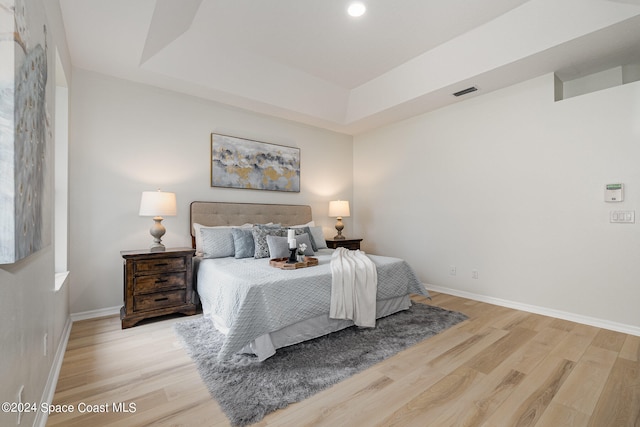 bedroom featuring a raised ceiling and light wood-type flooring