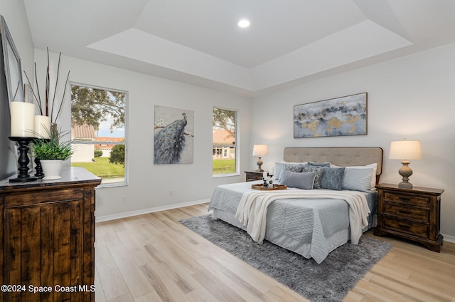 bedroom with a tray ceiling, multiple windows, and light wood-type flooring