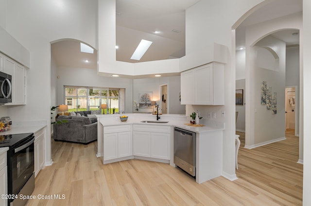 kitchen with sink, appliances with stainless steel finishes, high vaulted ceiling, and white cabinets