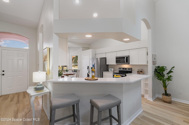 kitchen with kitchen peninsula, white cabinets, appliances with stainless steel finishes, high vaulted ceiling, and light hardwood / wood-style floors