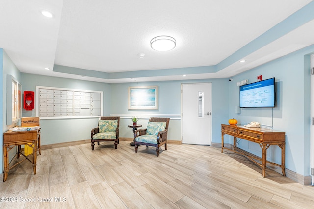 sitting room with light wood-type flooring, a raised ceiling, and a mail area