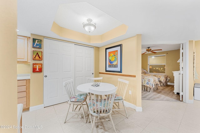 dining space featuring light tile patterned floors, a tray ceiling, and ceiling fan