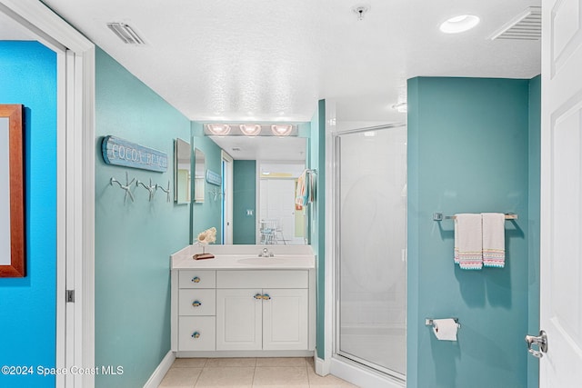 bathroom featuring vanity, a shower with shower door, tile patterned flooring, and a textured ceiling