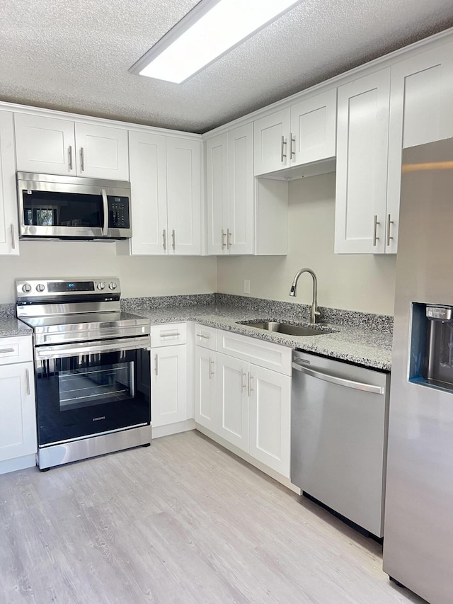 kitchen with light hardwood / wood-style floors, white cabinetry, appliances with stainless steel finishes, light stone counters, and sink