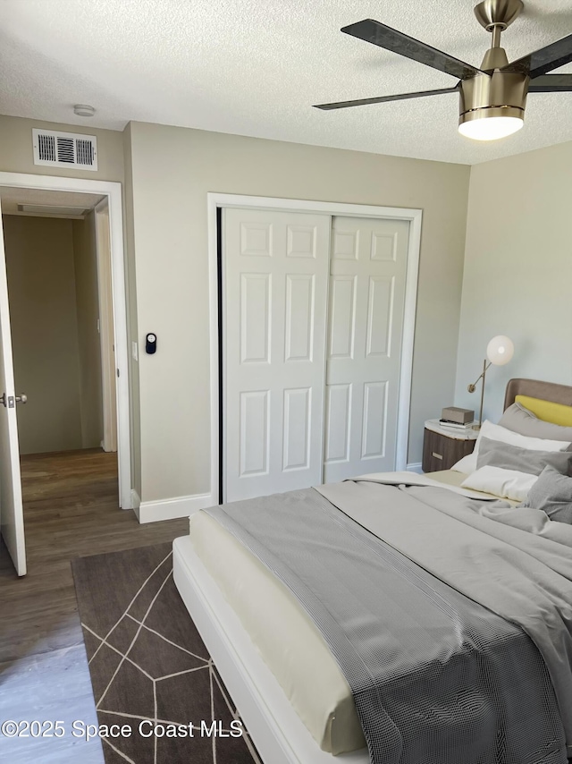 bedroom with ceiling fan, a textured ceiling, dark hardwood / wood-style floors, and a closet