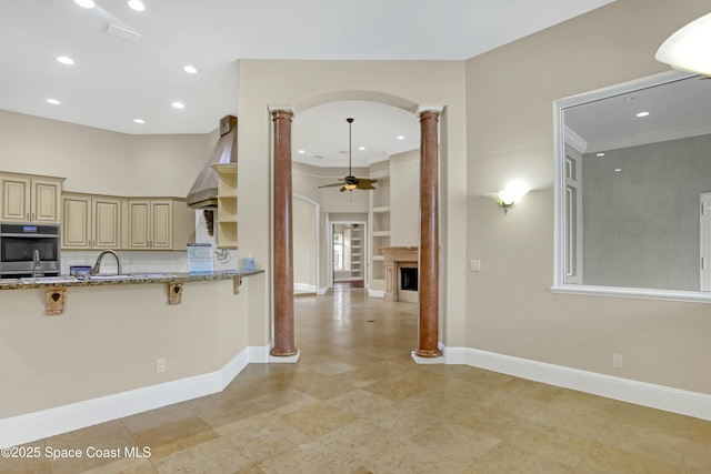 kitchen featuring ceiling fan, light stone counters, tasteful backsplash, cream cabinetry, and ornate columns