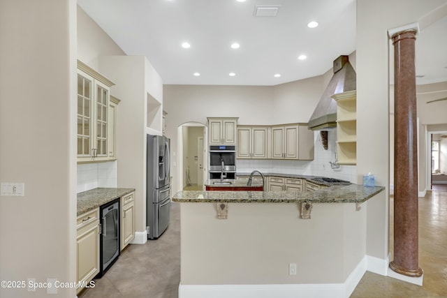 kitchen featuring stainless steel appliances, tasteful backsplash, cream cabinets, stone countertops, and kitchen peninsula