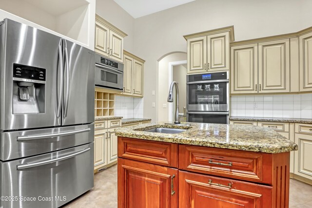 kitchen featuring appliances with stainless steel finishes, an island with sink, sink, decorative backsplash, and cream cabinets