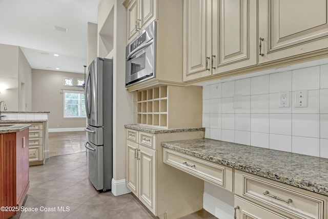 kitchen featuring light tile patterned floors, sink, stainless steel fridge, light stone countertops, and cream cabinetry