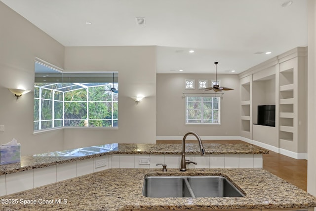 kitchen featuring pendant lighting, built in features, white cabinetry, sink, and light stone counters