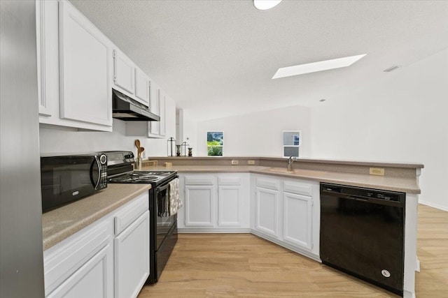 kitchen with light hardwood / wood-style flooring, kitchen peninsula, vaulted ceiling with skylight, white cabinets, and black appliances