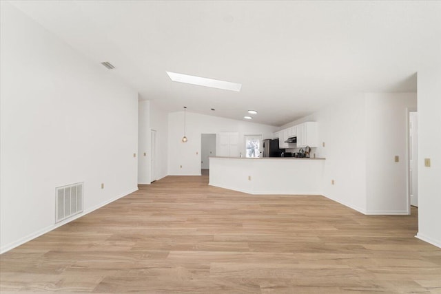 unfurnished living room with vaulted ceiling with skylight and light hardwood / wood-style flooring