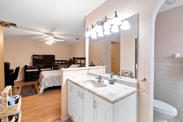 bathroom with ceiling fan, hardwood / wood-style flooring, tile walls, vanity, and toilet