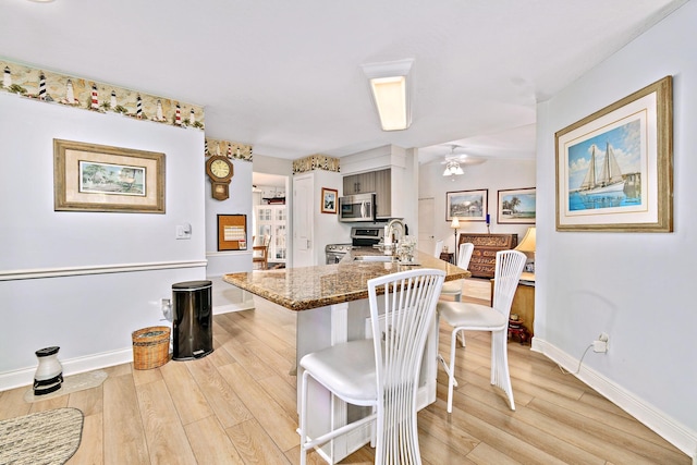 kitchen featuring stainless steel appliances, dark stone counters, light hardwood / wood-style floors, sink, and a breakfast bar