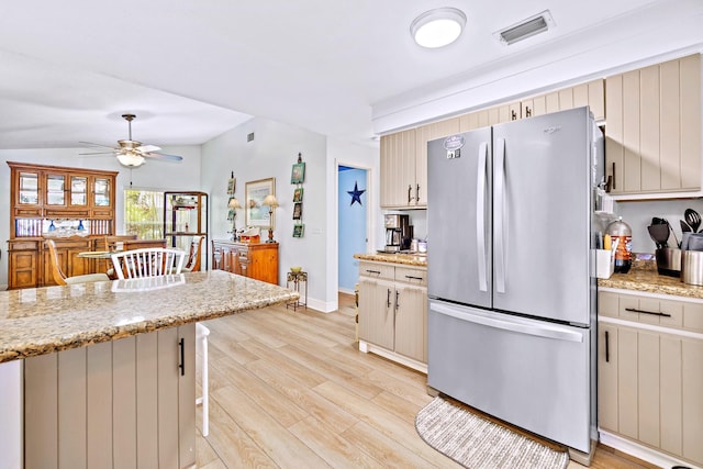 kitchen with ceiling fan, light stone counters, a breakfast bar, light hardwood / wood-style floors, and stainless steel refrigerator