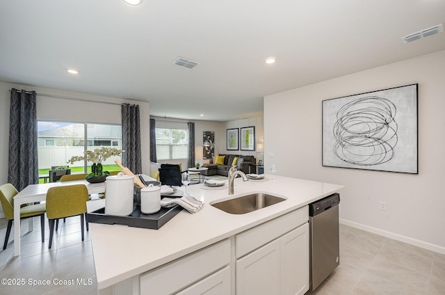 kitchen with sink, light tile patterned floors, a kitchen island with sink, white cabinets, and stainless steel dishwasher