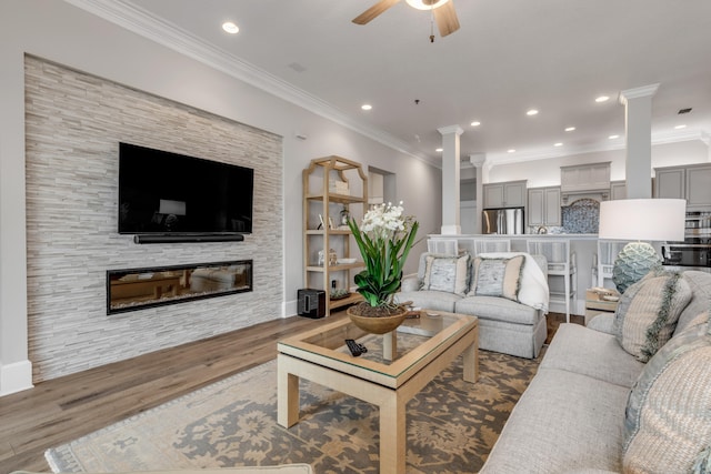 living room with a stone fireplace, ceiling fan, crown molding, decorative columns, and hardwood / wood-style flooring