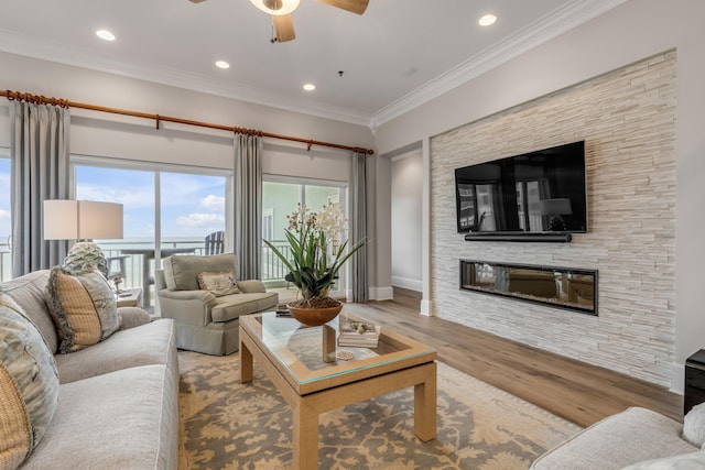 living room with crown molding, ceiling fan, a fireplace, and wood-type flooring