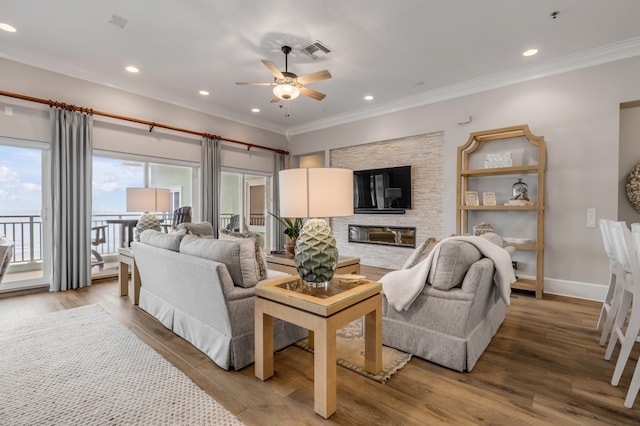 living room with ceiling fan, light hardwood / wood-style floors, a fireplace, and ornamental molding